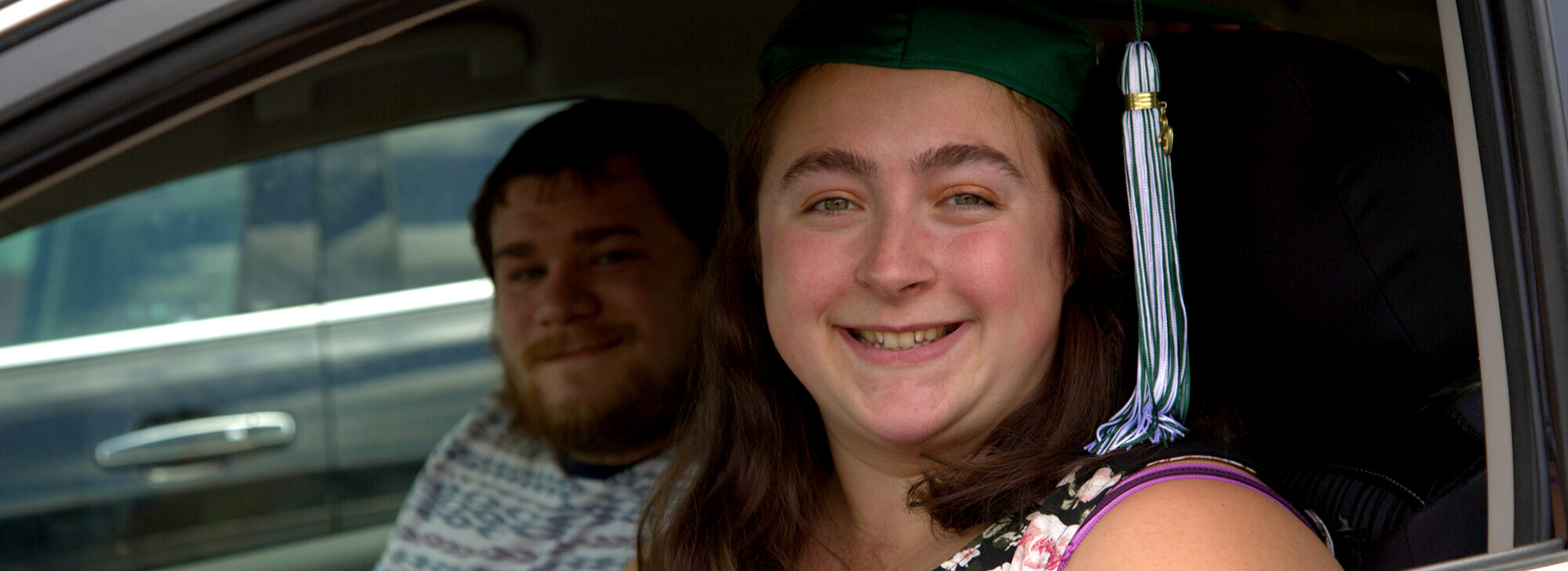 A graduate and guest attend the Norwich Campus's 2020 Drive-Thru Commencement from their vehicle