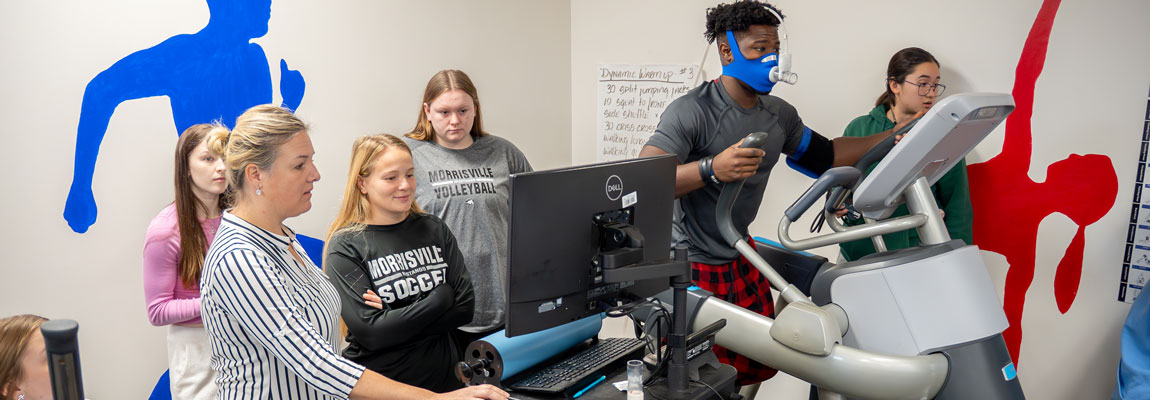 A group of students monitoring a computer while someone exercises on a machine