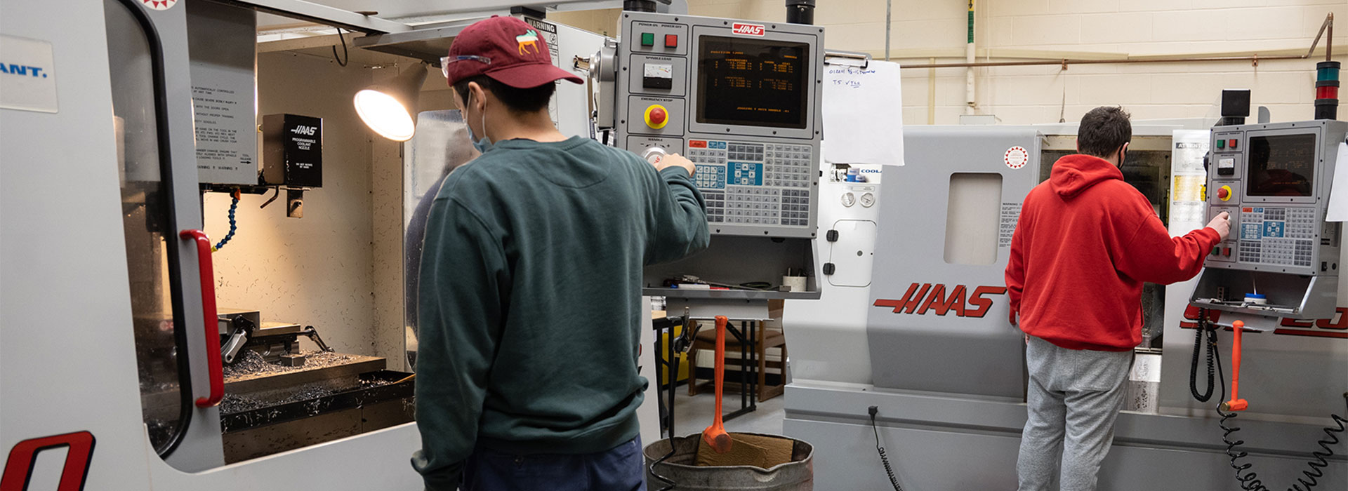 Two mechanical engineering students work with machining equipment in a lab.