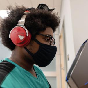 A SUNY Morrisville esports competitor sits in profile at a computer with headphones on.
