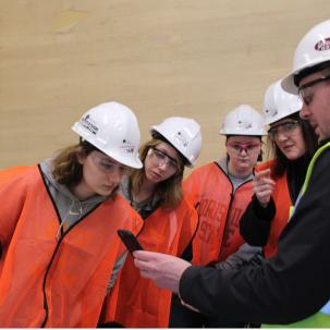 A faculty member and three students in the Architectural Studies and Design program visit a job site where the Project Manager (an alumnus of the program) shows them a detail of the building.